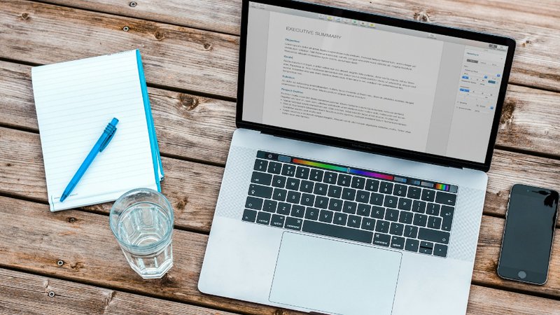 silver MacBook beside space gray iPhone 6 and clear drinking glass on brown wooden top